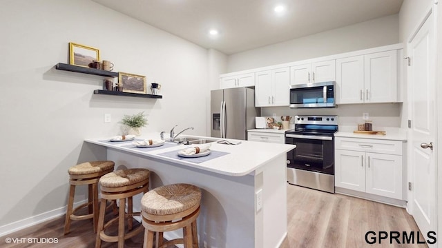 kitchen featuring light hardwood / wood-style floors, a breakfast bar, stainless steel appliances, sink, and white cabinetry