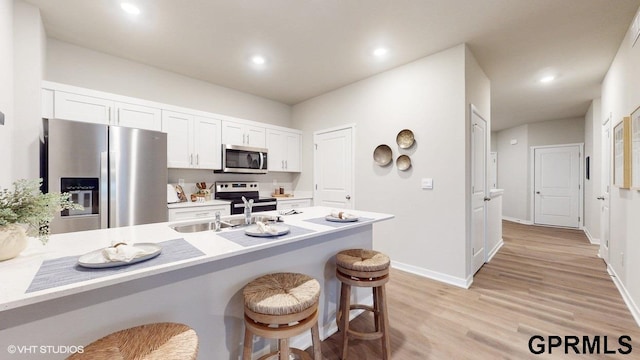 kitchen featuring light wood-type flooring, white cabinetry, stainless steel appliances, sink, and a breakfast bar area