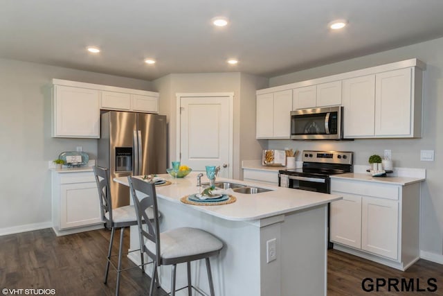 kitchen with appliances with stainless steel finishes, white cabinetry, an island with sink, and dark wood-type flooring