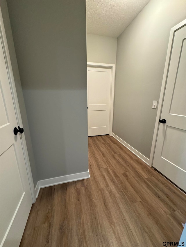 hall featuring baseboards, a textured ceiling, and wood finished floors