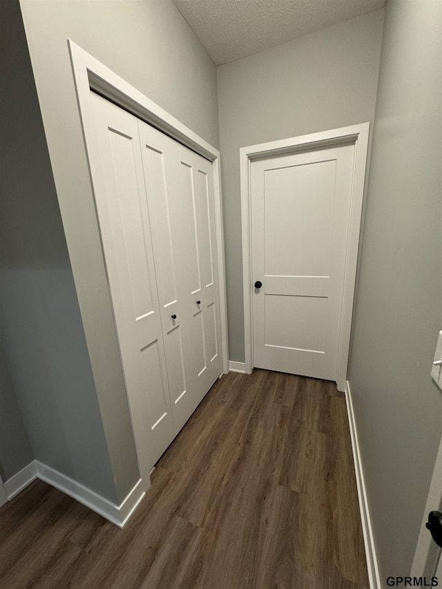 corridor featuring a textured ceiling, dark wood-style floors, and baseboards