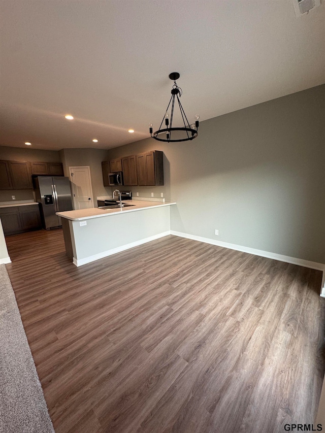 kitchen featuring an inviting chandelier, baseboards, a sink, a peninsula, and appliances with stainless steel finishes