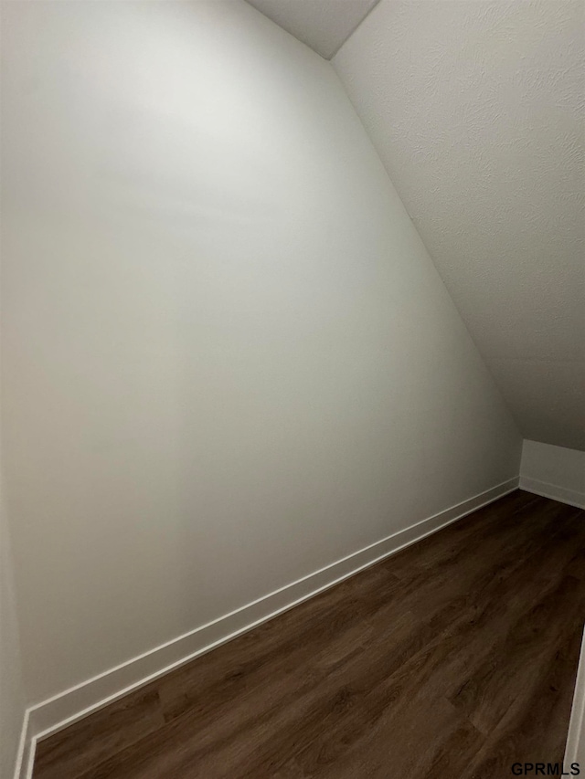 bonus room featuring baseboards, vaulted ceiling, and dark wood-style flooring