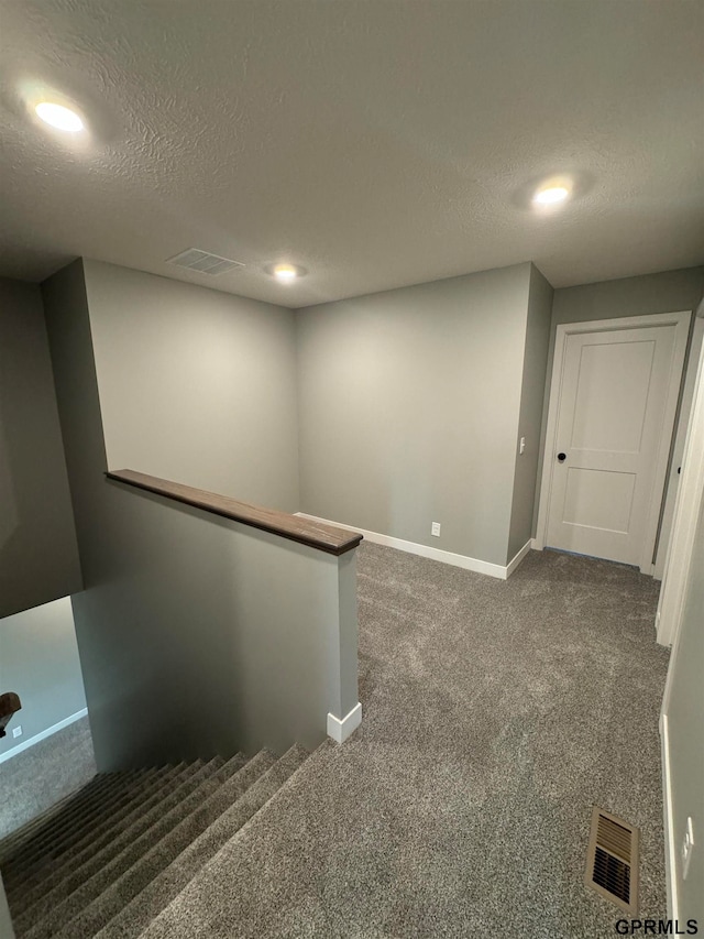 interior space featuring baseboards, visible vents, dark colored carpet, and a textured ceiling