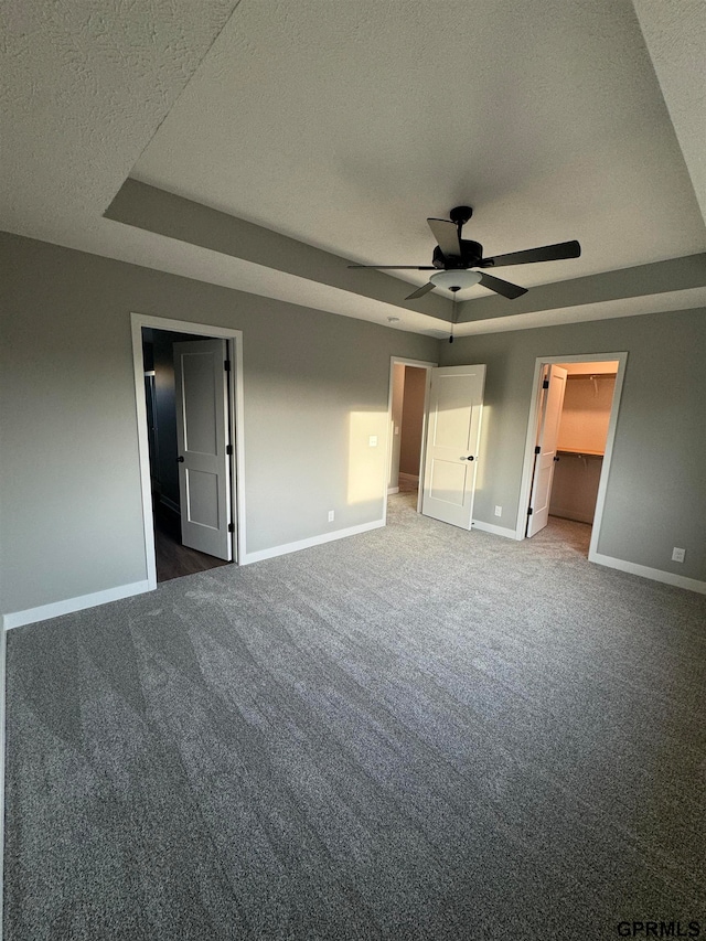 unfurnished bedroom with a tray ceiling, baseboards, carpet flooring, and a spacious closet