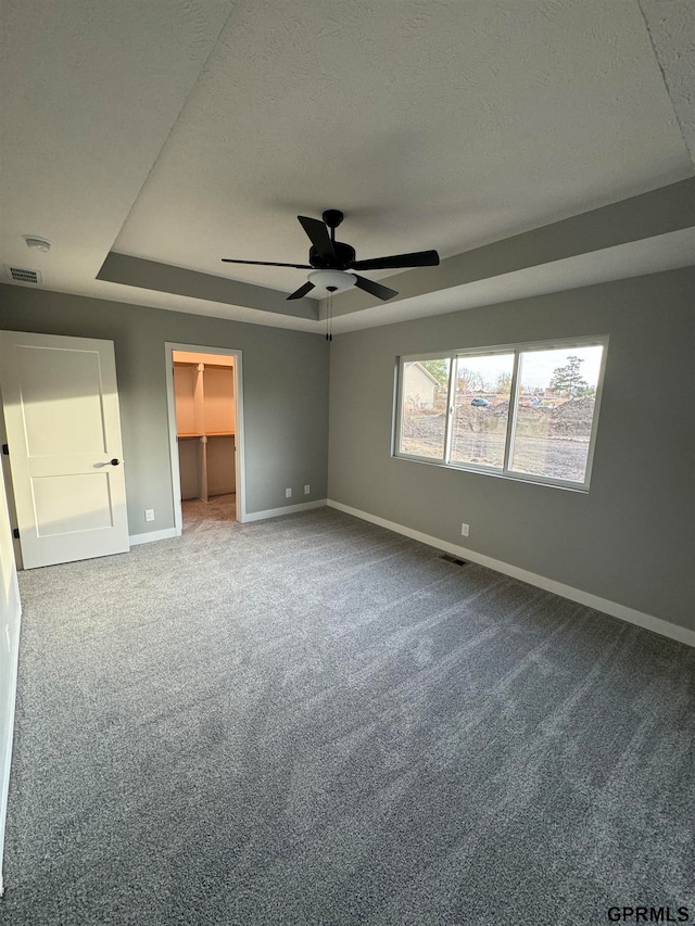 unfurnished bedroom with carpet flooring, visible vents, baseboards, a tray ceiling, and a walk in closet
