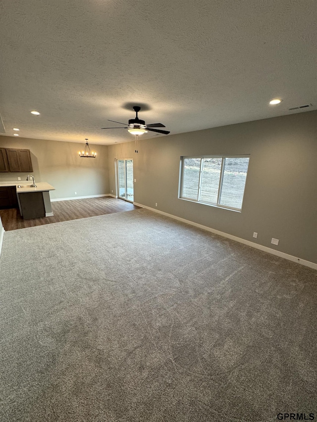 unfurnished living room with baseboards, a sink, and ceiling fan with notable chandelier