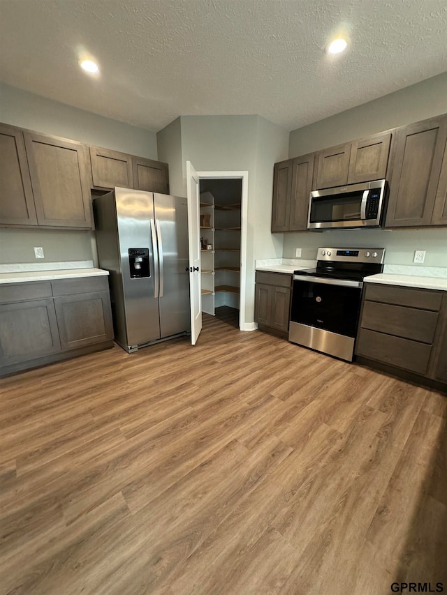 kitchen with a textured ceiling, light countertops, light wood-style flooring, and stainless steel appliances