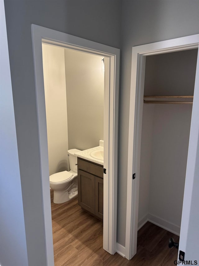 half bath with toilet, wood finished floors, baseboards, and vanity