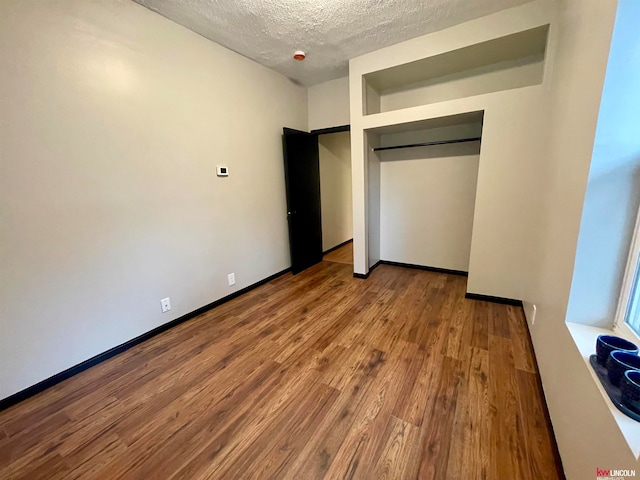 unfurnished bedroom with a textured ceiling, a closet, and hardwood / wood-style floors