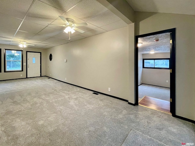 carpeted empty room with a wealth of natural light, ceiling fan, and a drop ceiling