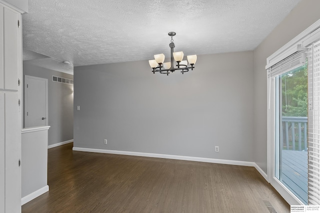 empty room featuring a textured ceiling, a chandelier, and dark hardwood / wood-style floors