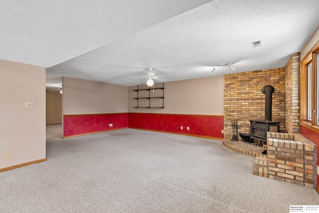 unfurnished living room with a textured ceiling, ceiling fan, a wood stove, and carpet flooring