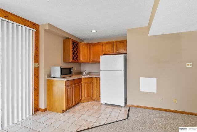 kitchen with wooden walls, a textured ceiling, sink, white refrigerator, and light colored carpet