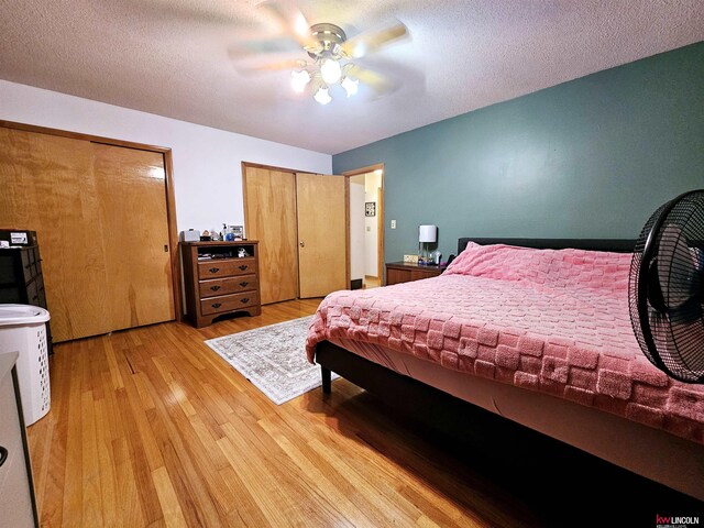 bedroom featuring multiple closets, a textured ceiling, light wood-style flooring, and a ceiling fan
