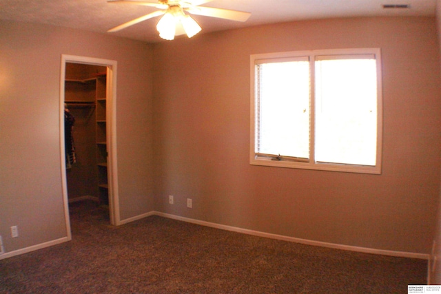 unfurnished bedroom with dark carpet, a closet, ceiling fan, and a spacious closet