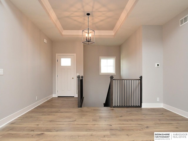 entryway with light wood-type flooring, an inviting chandelier, a raised ceiling, and crown molding