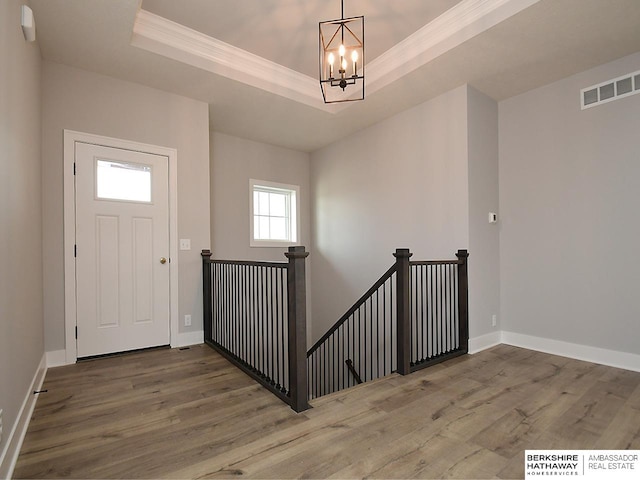 entrance foyer with crown molding, a tray ceiling, an inviting chandelier, and hardwood / wood-style flooring