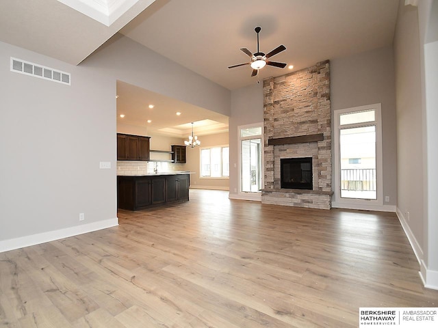 unfurnished living room featuring a fireplace, ceiling fan with notable chandelier, plenty of natural light, and light hardwood / wood-style flooring