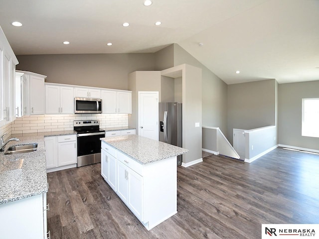 kitchen with dark wood finished floors, lofted ceiling, a sink, appliances with stainless steel finishes, and a center island