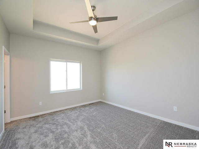 carpeted empty room with a raised ceiling, a ceiling fan, and baseboards