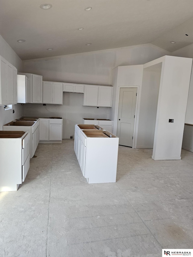 kitchen with a sink, a kitchen island, recessed lighting, white cabinets, and vaulted ceiling