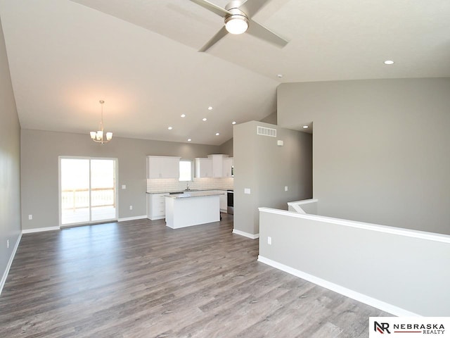 unfurnished living room with baseboards, visible vents, dark wood finished floors, lofted ceiling, and ceiling fan with notable chandelier