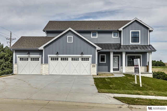 view of front of property with an attached garage, board and batten siding, a front yard, a standing seam roof, and stone siding