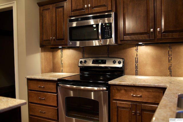 kitchen featuring light stone countertops, stainless steel appliances, and dark brown cabinets