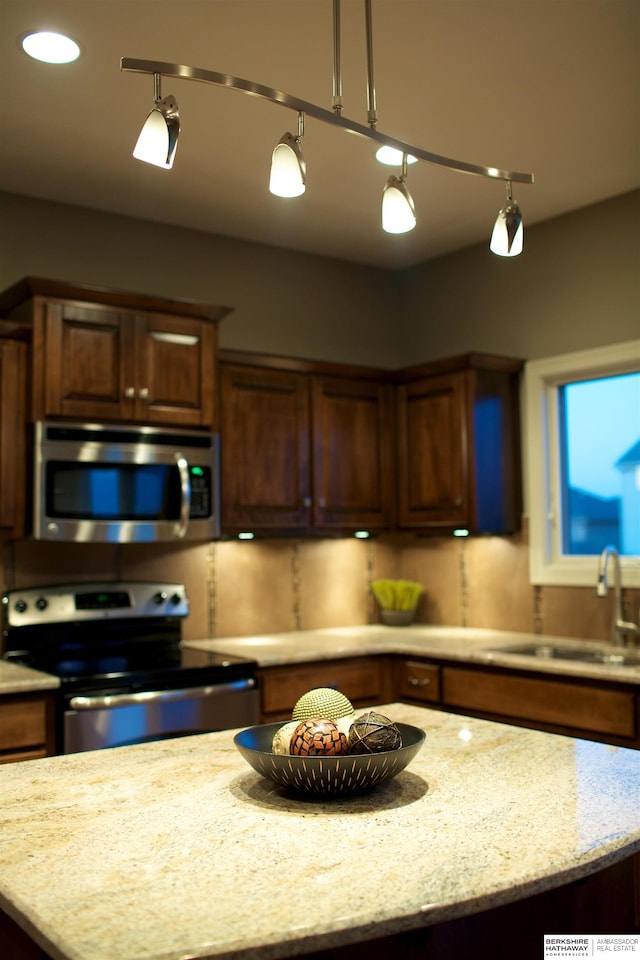 kitchen featuring stainless steel appliances, sink, decorative light fixtures, and light stone countertops