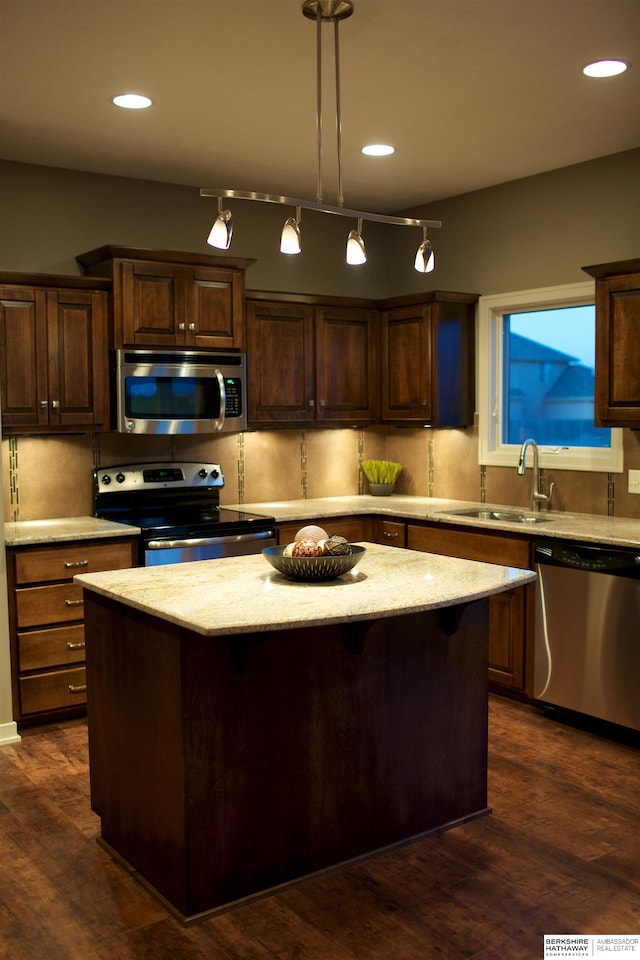 kitchen featuring stainless steel appliances, decorative light fixtures, a kitchen island, sink, and dark wood-type flooring