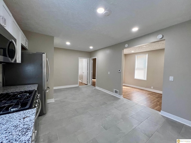 kitchen with white cabinets, stainless steel appliances, light stone countertops, and a textured ceiling