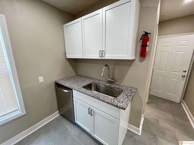 kitchen with light tile patterned floors, sink, stainless steel dishwasher, white cabinets, and light stone countertops