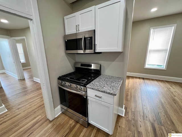 kitchen featuring light wood-type flooring, stainless steel appliances, white cabinetry, and light stone countertops