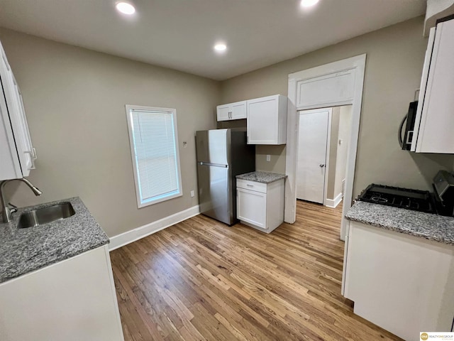 kitchen with white cabinets, sink, light stone countertops, and stainless steel fridge