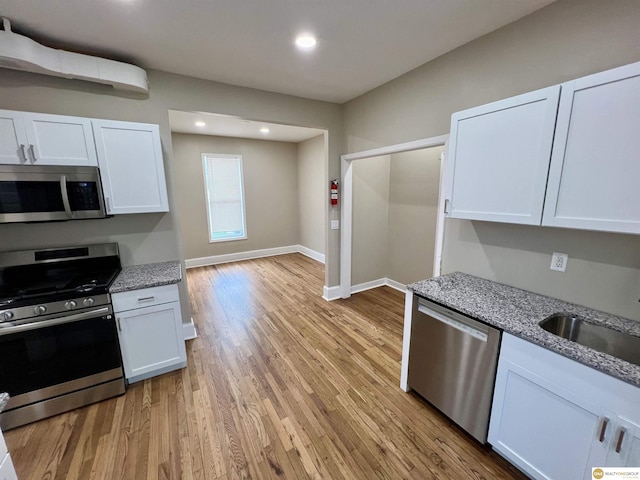 kitchen with white cabinets, light hardwood / wood-style floors, appliances with stainless steel finishes, and light stone counters