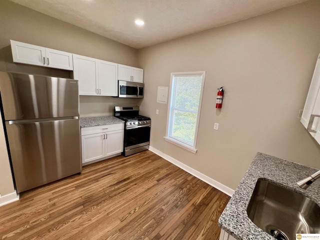 kitchen featuring white cabinetry, sink, stainless steel appliances, and light stone counters