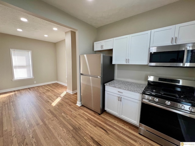 kitchen featuring white cabinetry, stainless steel appliances, light stone countertops, light hardwood / wood-style floors, and a textured ceiling