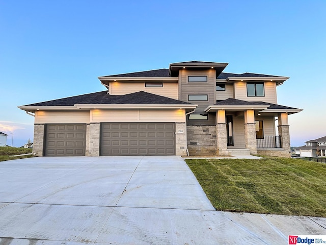 prairie-style home featuring driveway, covered porch, stone siding, and a front yard