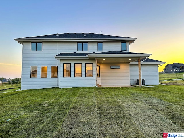 back of house at dusk with a yard and central AC unit