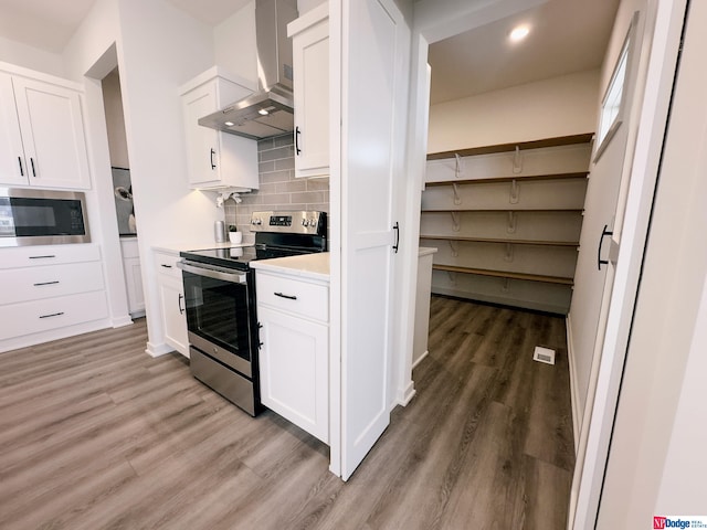 kitchen featuring light countertops, appliances with stainless steel finishes, white cabinets, wood finished floors, and wall chimney exhaust hood