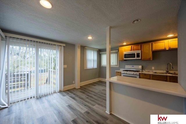 kitchen with a textured ceiling, white range with gas stovetop, sink, and light hardwood / wood-style flooring