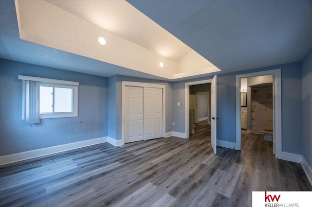 unfurnished bedroom with dark wood-type flooring, a textured ceiling, vaulted ceiling, and a closet