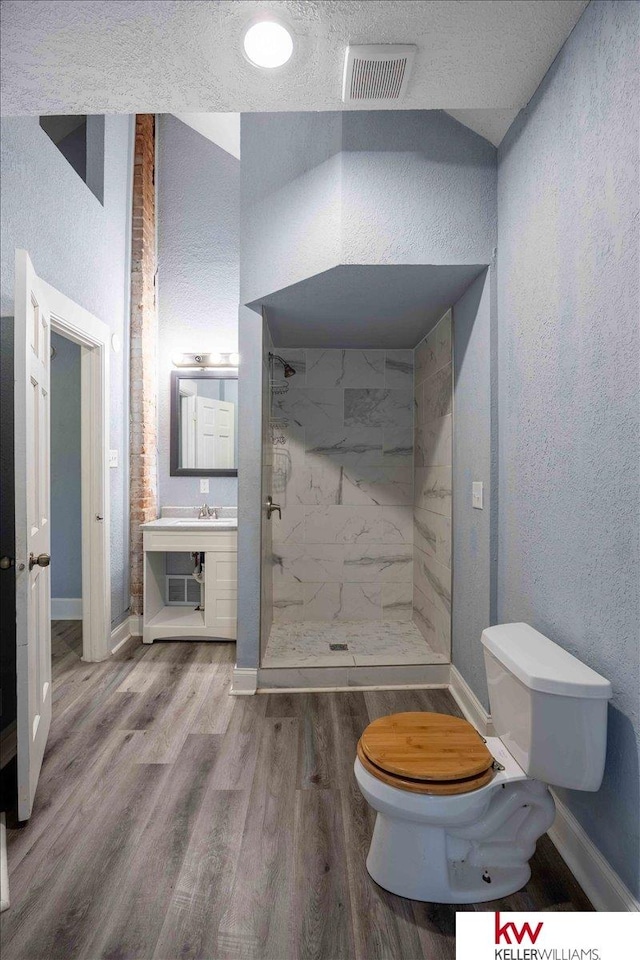 bathroom with toilet, a textured ceiling, a tile shower, hardwood / wood-style flooring, and vanity