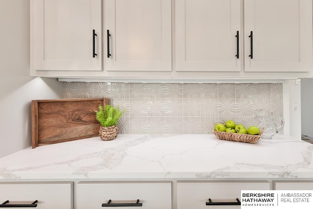 room details with light stone counters, decorative backsplash, and white cabinetry