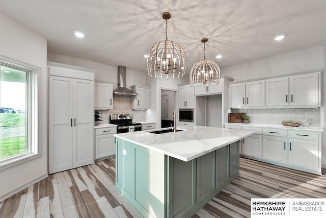 kitchen featuring light stone countertops, a center island with sink, stainless steel appliances, sink, and wall chimney range hood