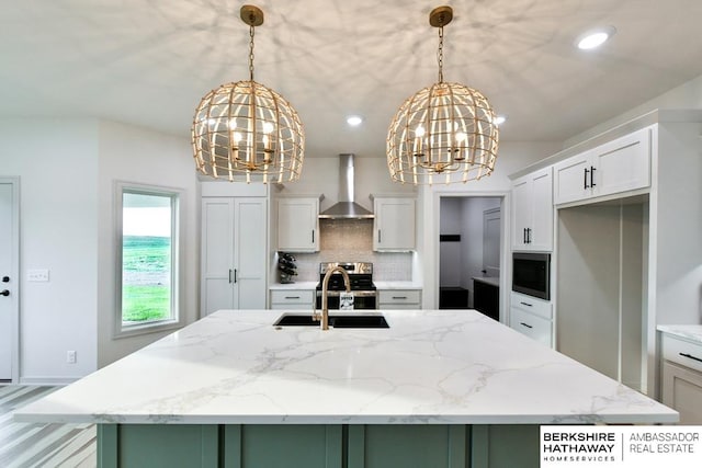 kitchen featuring decorative light fixtures, wall chimney range hood, and a kitchen island with sink