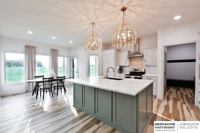 kitchen with decorative light fixtures, wall chimney exhaust hood, light hardwood / wood-style floors, sink, and electric stove