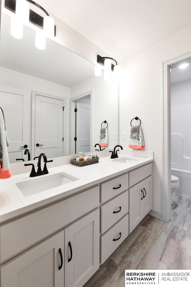 bathroom featuring toilet, a tub to relax in, vanity, a textured ceiling, and hardwood / wood-style flooring