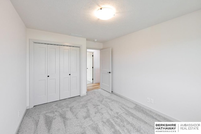 unfurnished bedroom with a textured ceiling, light colored carpet, and a closet